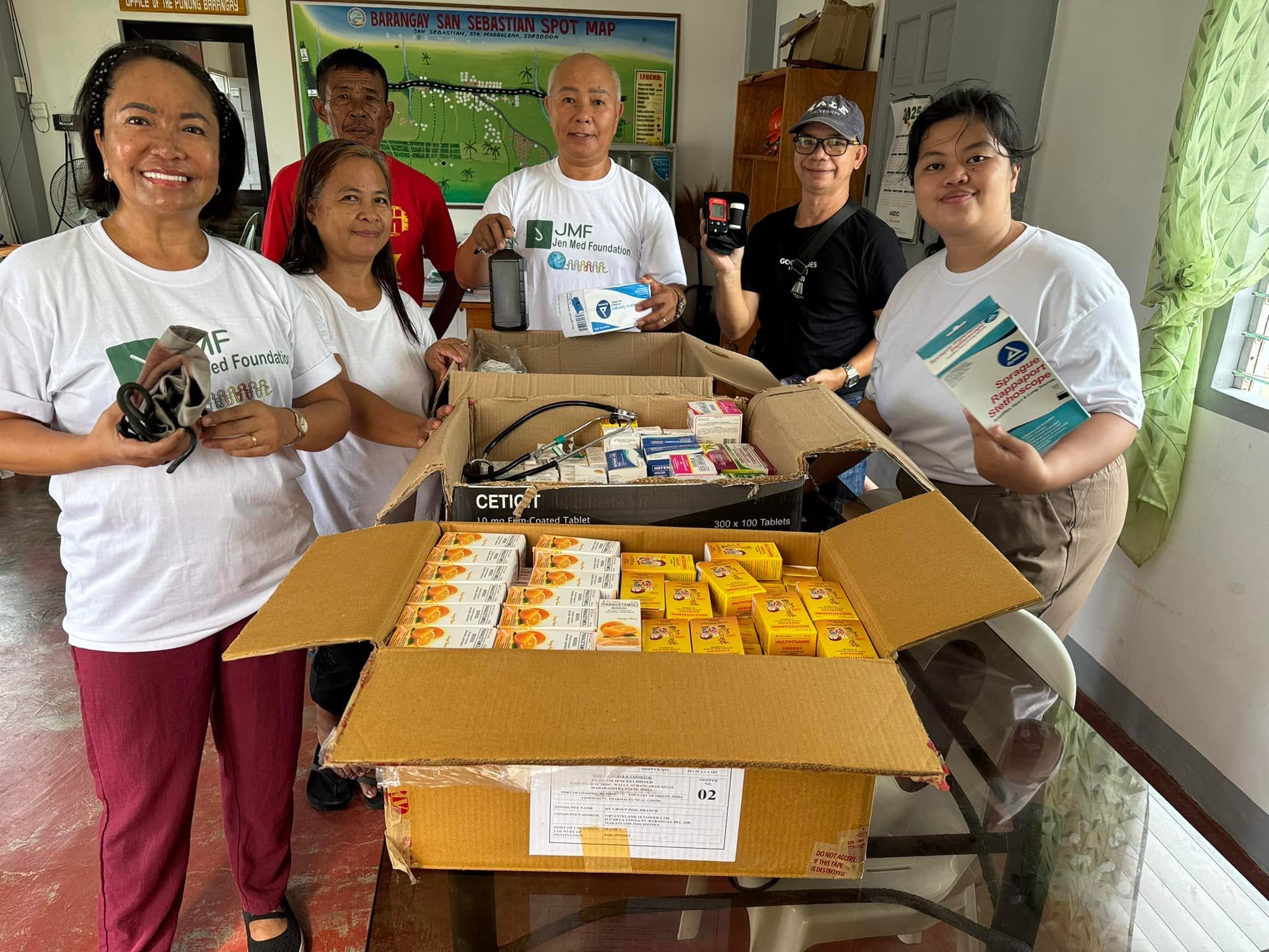A group stands behind open boxes of medicines and medical supplies.