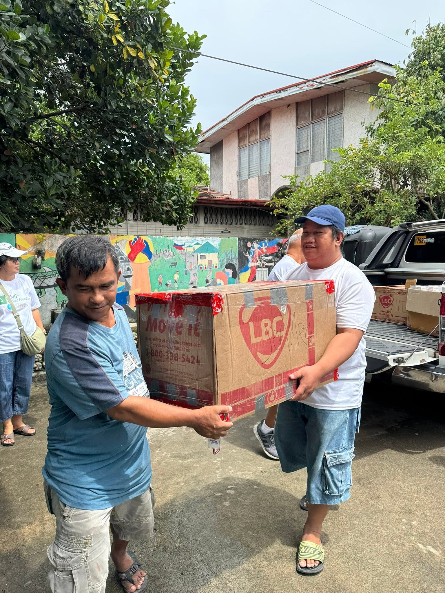 Two people carry a large donation box outdoors.