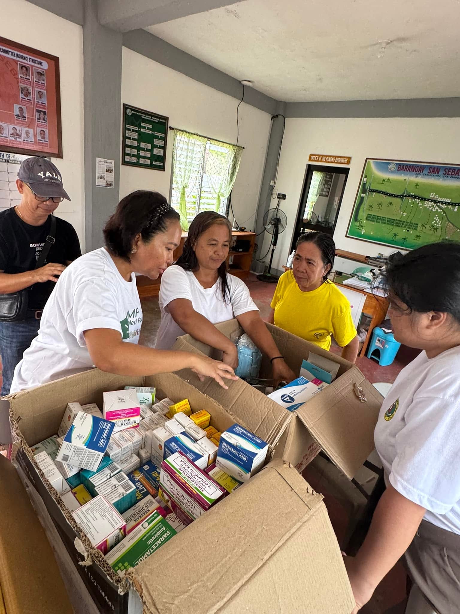 Volunteers discuss and sort medicines in open boxes.