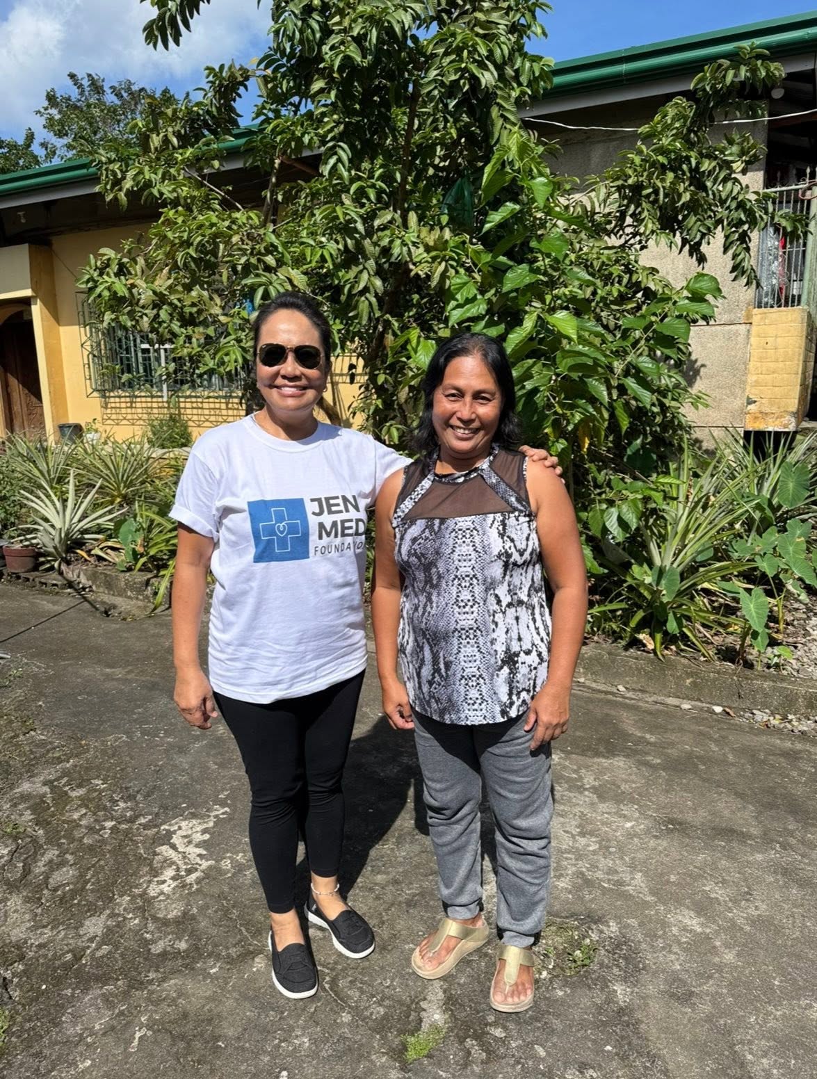 Two smiling people stand outdoors, one wearing a JenMed Foundation shirt.