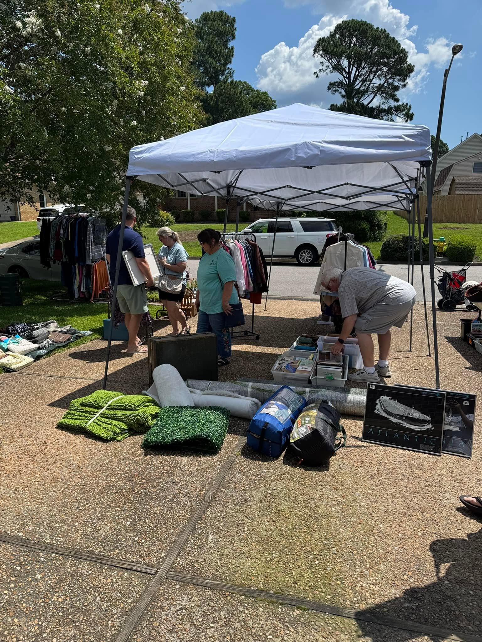 People browse donated goods beneath a canopy at an outdoor sale.