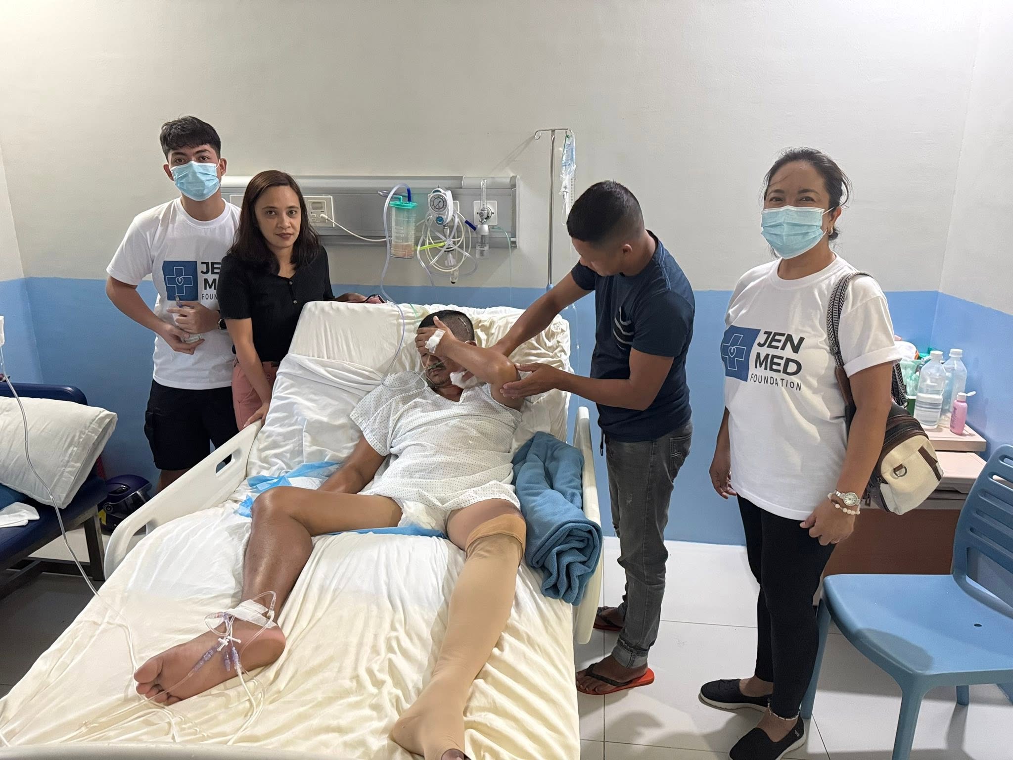 A patient receives bedside assistance while JenMed volunteers stand nearby.