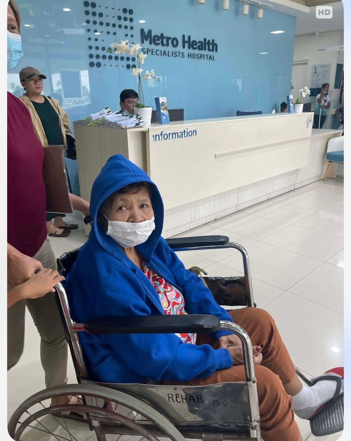 A person using a wheelchair is accompanied at a hospital reception desk.